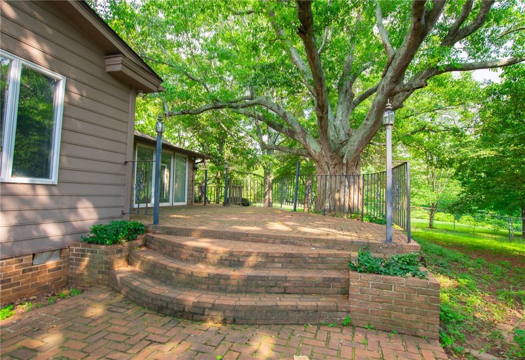 200 Chenault Road Townville, SC 29689 - Photo 34 of 47 An inviting brick patio extends from the house, offering a private outdoor space for relaxation amidst lush greenery.