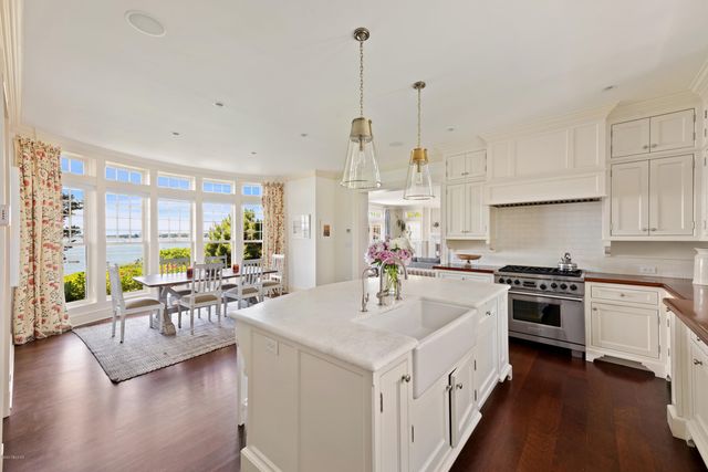 a kitchen with stainless steel appliances granite countertop a stove top oven a sink a dining table and chairs with wooden floor