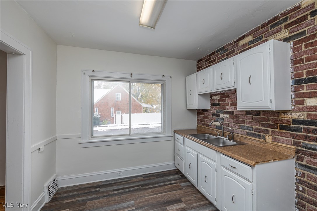 6003 Snow Road Parma, OH 44129 - Photo 3 of 28 Kitchen featuring dark countertops, white cabinetry, dark wood-style flooring, and brick wall