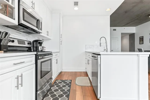 a kitchen with stainless steel appliances a refrigerator a stove a sink and white cabinets with wooden floor