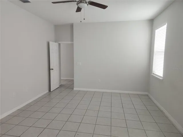 an empty room with chandelier fan and windows