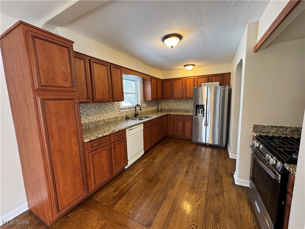 904 Trebisky Road Cleveland, OH 44121 - Photo 7 of 11 Kitchen with backsplash, appliances with stainless steel finishes, dark wood-type flooring, a sink, and light stone countertops