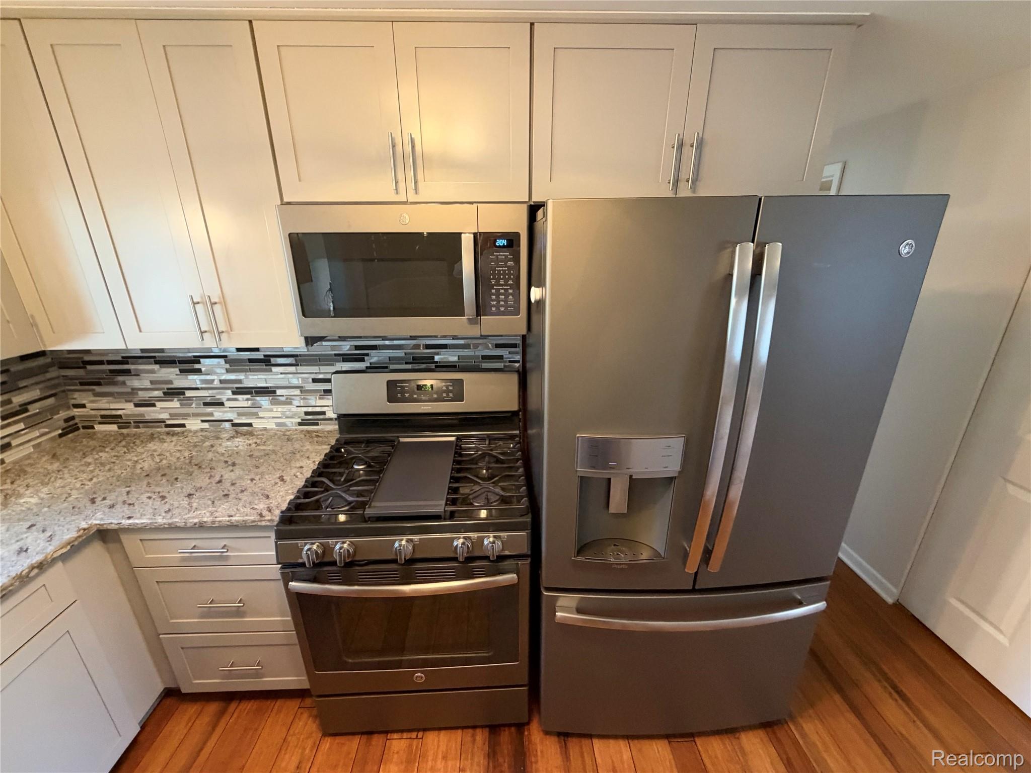 14629 Newburgh Road Livonia, MI 48154 - Photo 4 of 27 Stainless steel appliances, light-toned cabinetry, granite countertops, tile backsplash, and wood-finish flooring