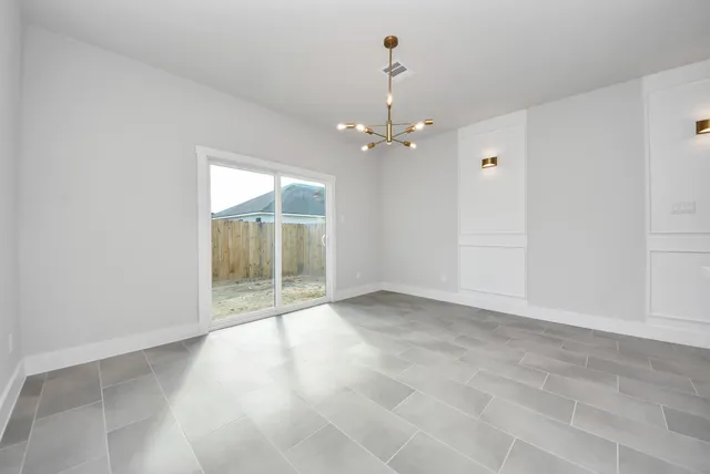 an empty room with chandelier fan and windows