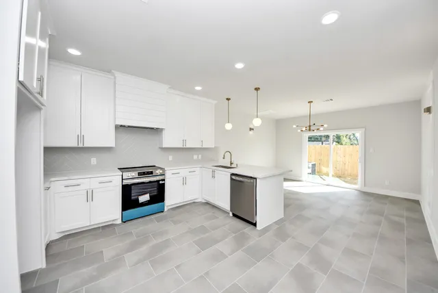 a large kitchen with stainless steel appliances granite countertop a stove a sink a refrigerator and white cabinets