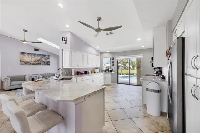 a open kitchen with stainless steel appliances granite countertop a refrigerator a sink dishwasher a dining table and chairs with white cabinets