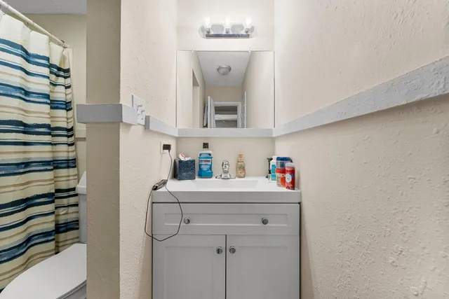 a view of small white house with a big yard plants and large tree