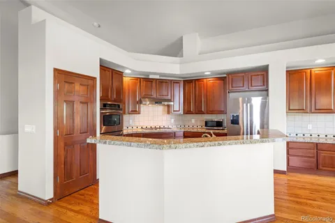 a kitchen with stainless steel appliances granite countertop a refrigerator a sink dishwasher a stove and white countertops with wooden floor