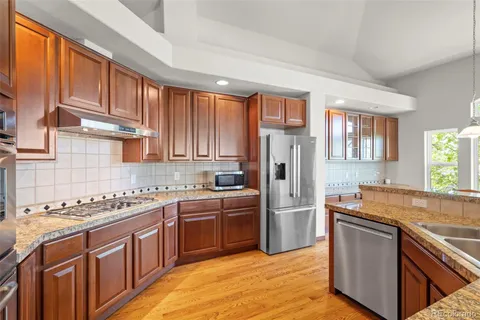 a kitchen with stainless steel appliances granite countertop a refrigerator a sink dishwasher a stove with wooden cabinets and floor