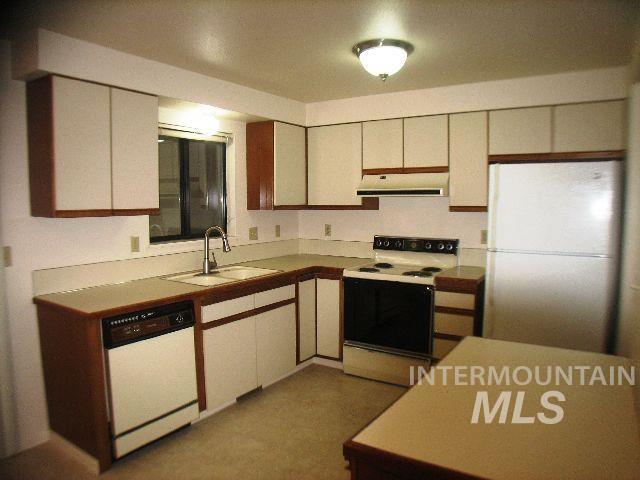 Kitchen with white appliances, light countertops, brown cabinetry, and under cabinet range hood