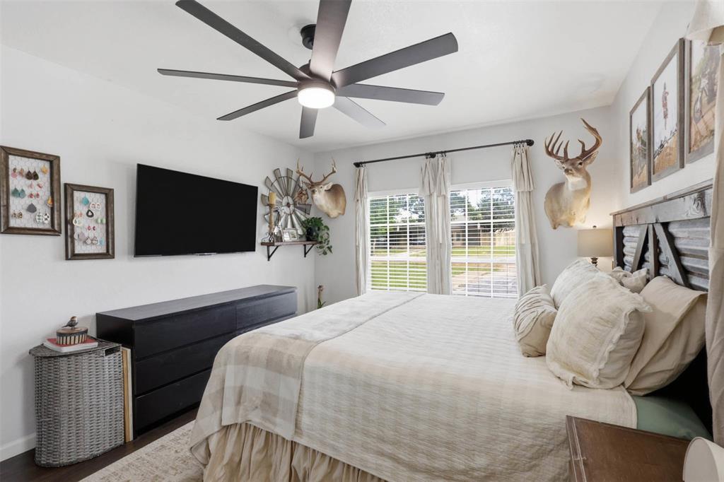 308 West 1st Street Springtown, TX 76082 - Photo 22 of 39 Spacious bedroom featuring multiple windows, a ceiling fan with integrated lighting, dark wood-finish flooring, and a mounted flat-screen television