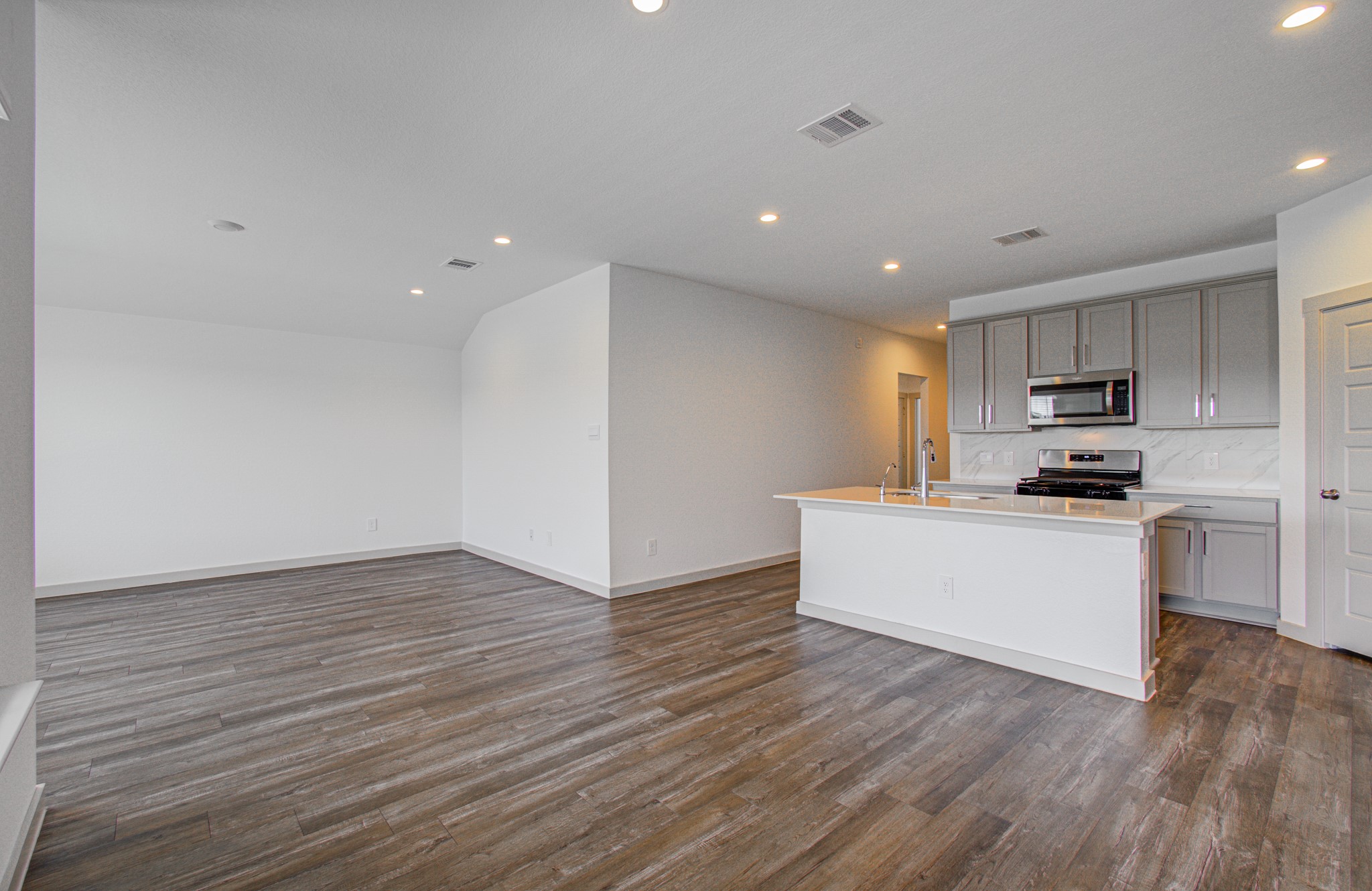 7903 Wrangler Shack Lane Rosharon, TX 77583 - Photo 18 of 29 Experience modern living in this bright, open-concept kitchen and living area, featuring sleek wood flooring, stainless steel appliances, a spacious island, and ample cabinets, all illuminated by elegant recessed lighting and set against neutral walls.