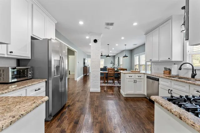 a kitchen with stainless steel appliances kitchen island granite countertop a refrigerator oven a sink dishwasher and white cabinets with wooden floor