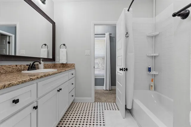a bathroom with a granite countertop sink a mirror a bathtub and shower