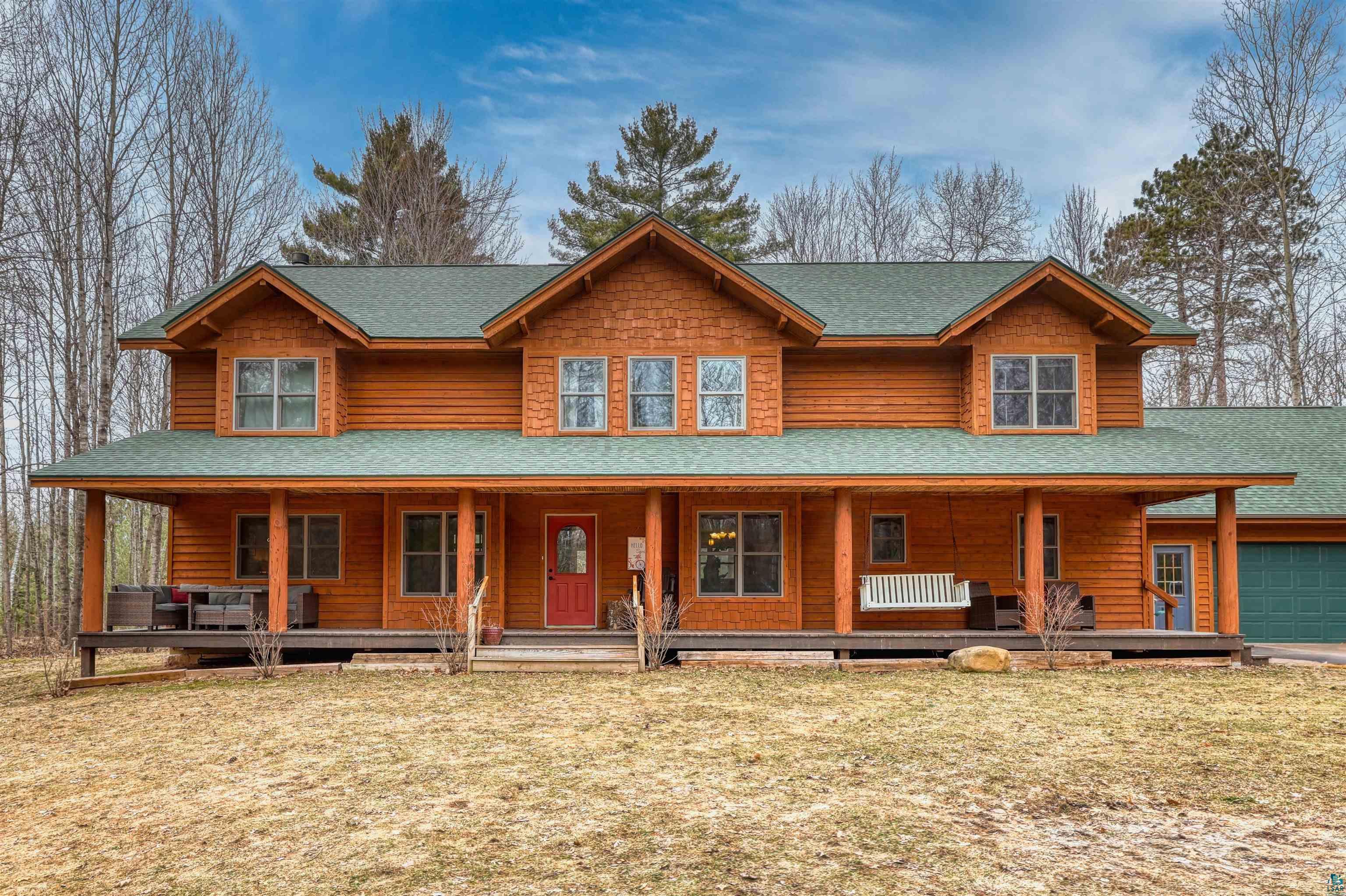 View of front of property with covered porch, a front yard, a shingled roof, and a garage