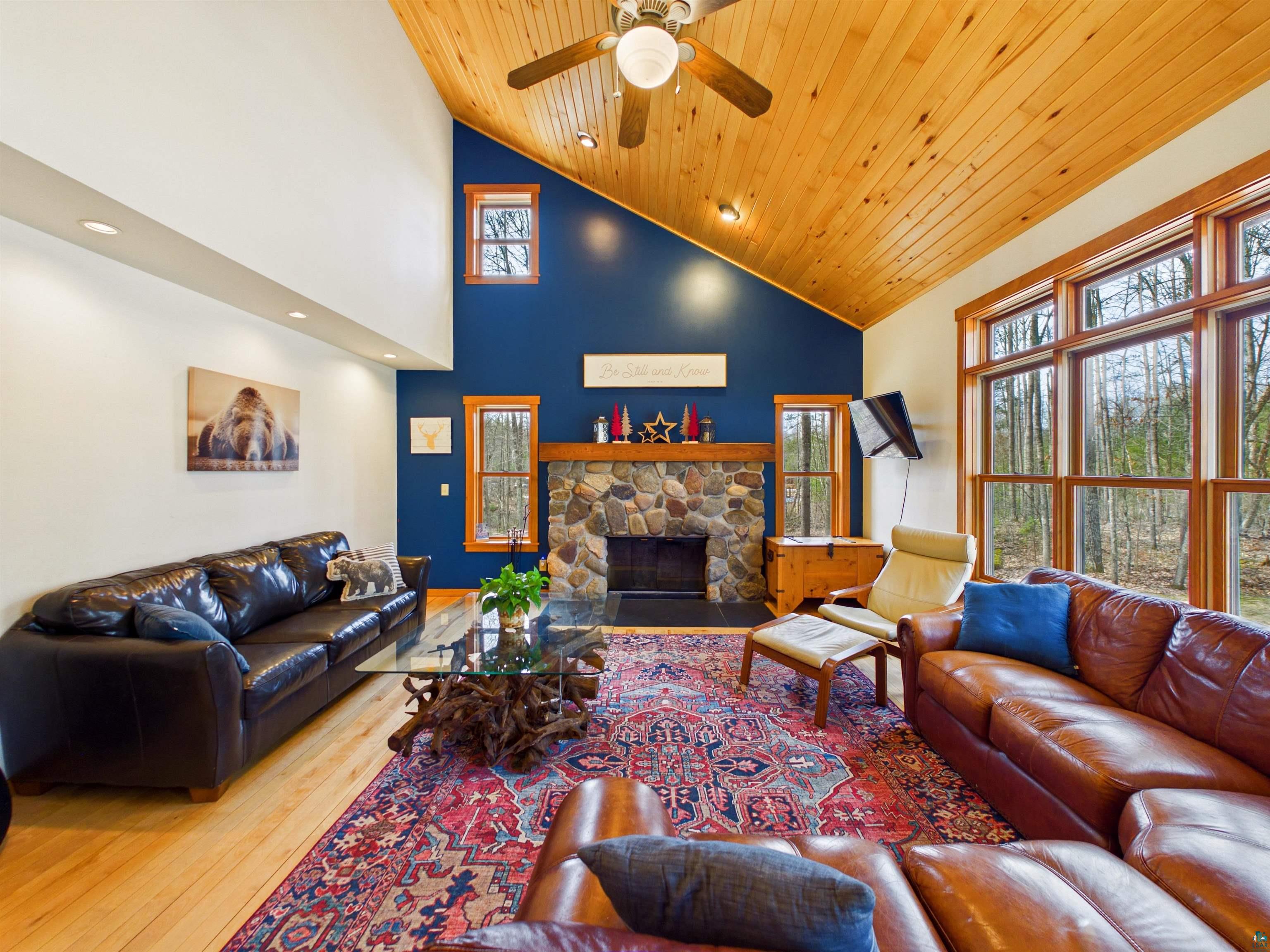 16539 Acorn Ridge Hayward, WI 54843 - Photo 19 of 58 Living room with wood-type flooring, a ceiling fan, a stone fireplace, lofted ceiling, and plenty of natural light