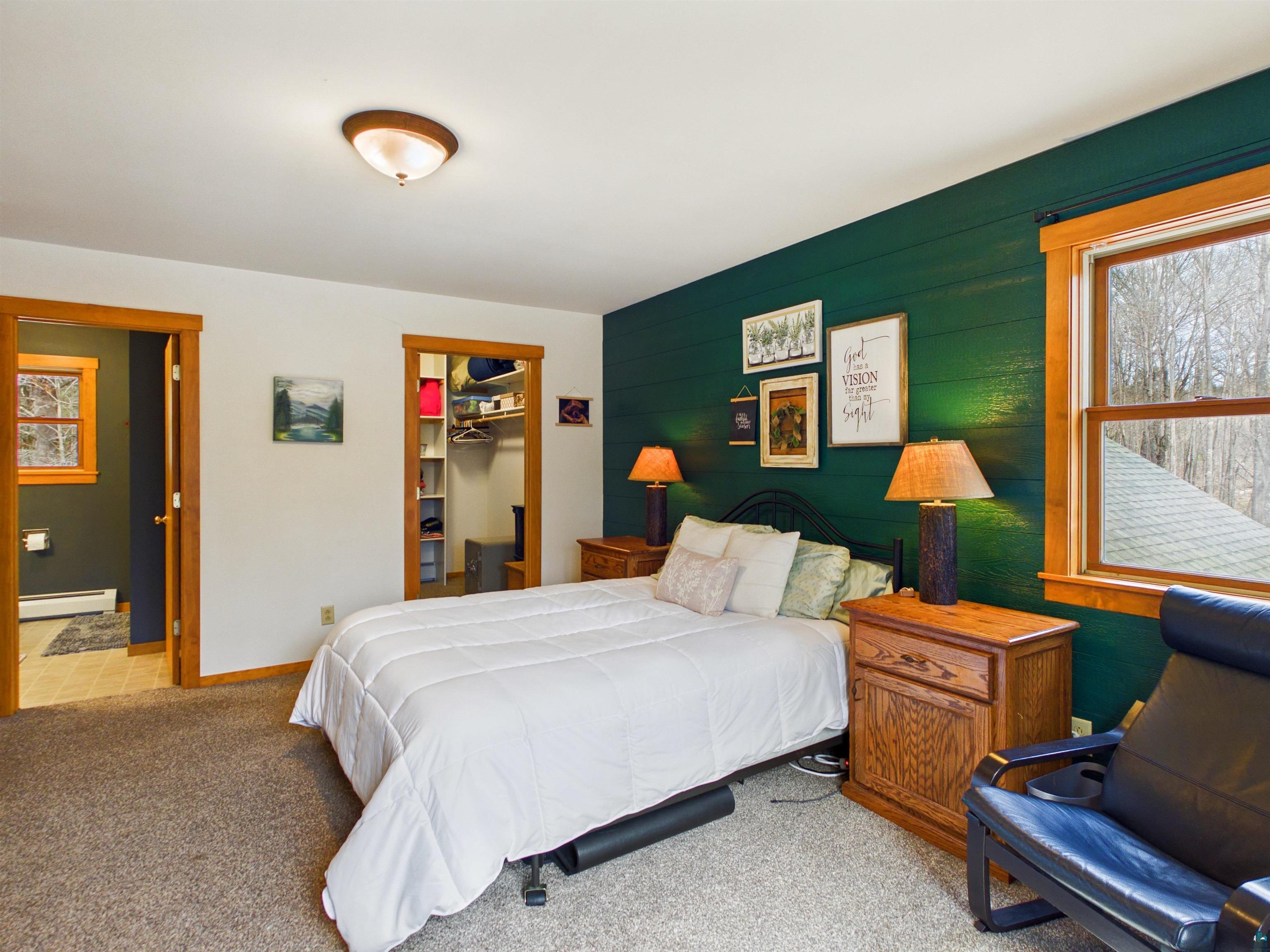 16539 Acorn Ridge Hayward, WI 54843 - Photo 36 of 58 Bedroom with light colored carpet, multiple windows, a baseboard heating unit, a walk in closet, and wood walls