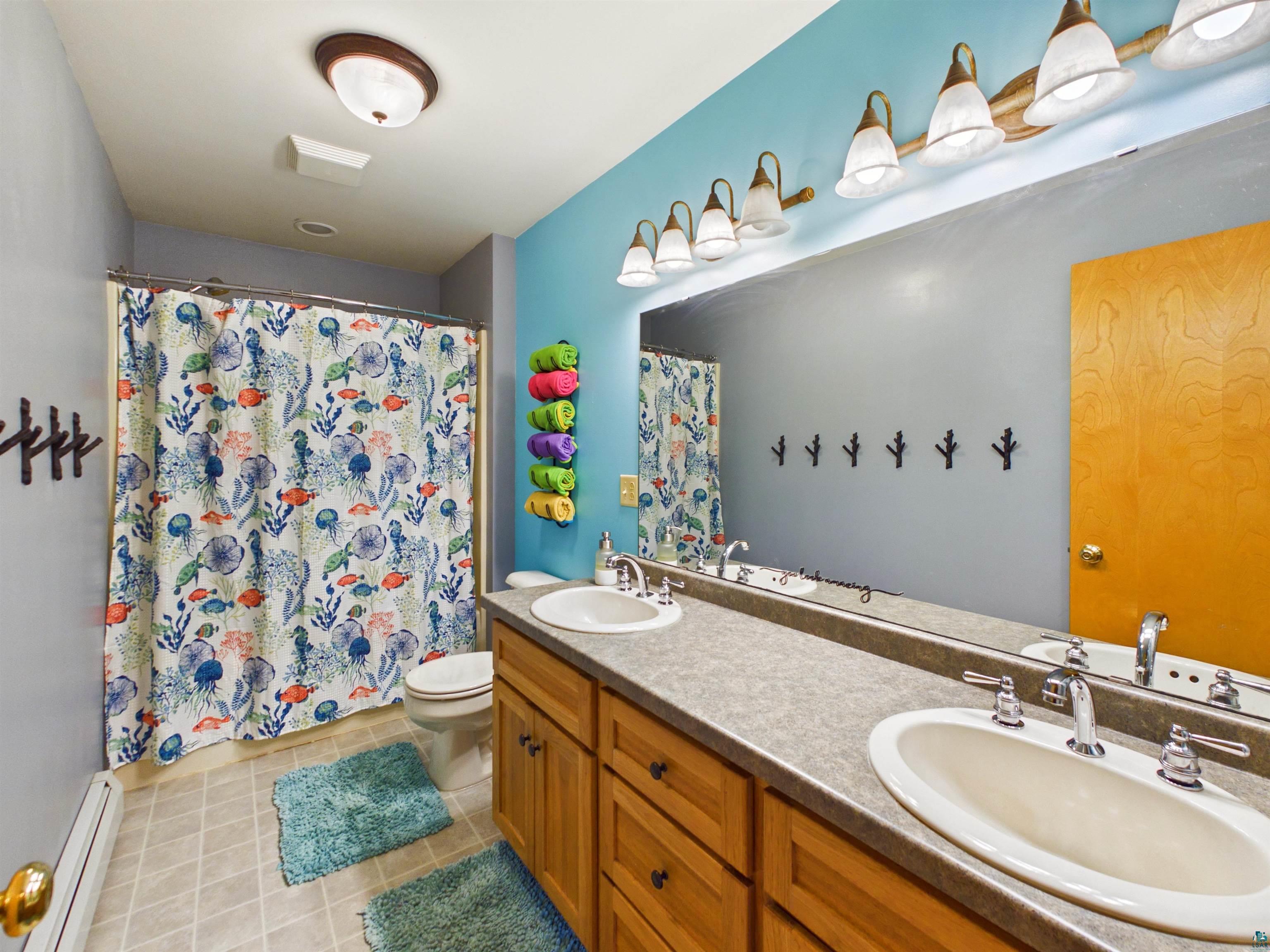 16539 Acorn Ridge Hayward, WI 54843 - Photo 43 of 58 Full bath with double vanity, a baseboard radiator, curtained shower, and light tile patterned flooring