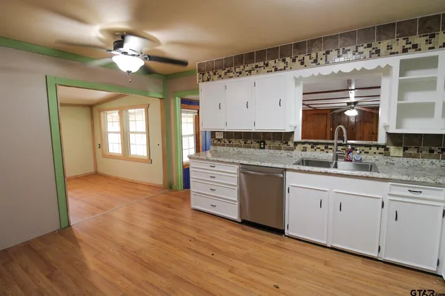 a kitchen with granite countertop a stove a sink and white cabinets with wooden floor