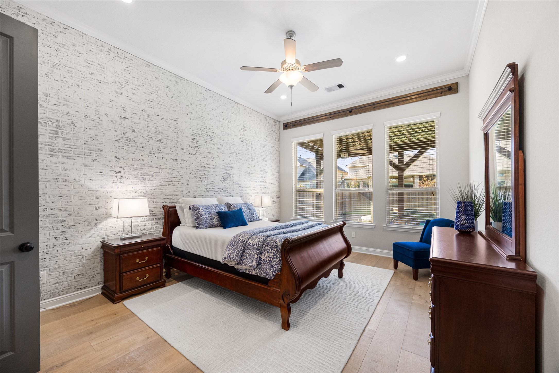 4320 Silver Oak Place Spring, TX 77386 - Photo 11 of 42 Primary bedroom located downstairs, showcasing a stylish faux brick accent wall and large windows that overlook the backyard, filling the space with natural light.