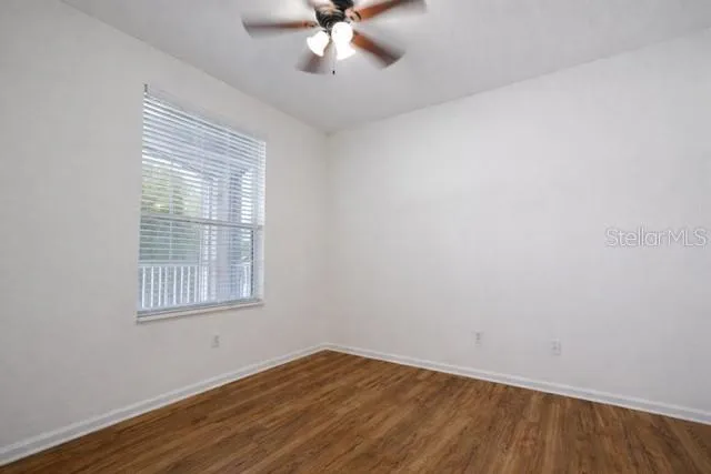 an empty room with wooden floor fan and windows
