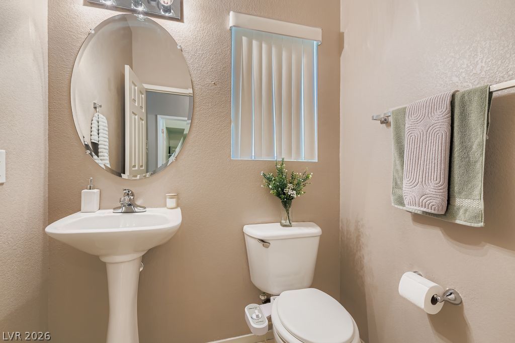 1586 Rusty Ridge Lane Henderson, NV 89002 - Photo 7 of 11 A well-appointed powder room features a pedestal sink, toilet, and an oval mirror, offering a refined space.