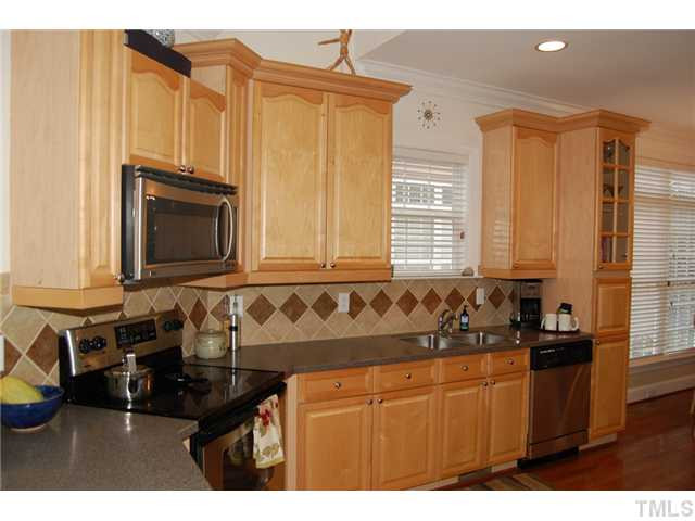 1148 Harp Street Raleigh, NC 27604 - Photo 2 of 23 Raised panel wood cabinetry trimmed with upgraded crown moldings and glass door display cabinet add warmth to this generous kitchen. Double door pantry with laundry space are on the wall to the right, adjacent to the stainless fridge. Kitchen