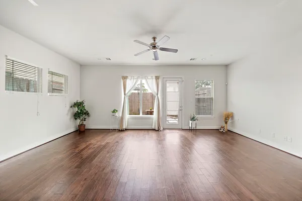 an empty room with wooden floor chandelier fan and windows