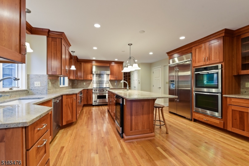 a kitchen with stainless steel appliances kitchen island granite countertop wooden floor a stove a sink and a refrigerator