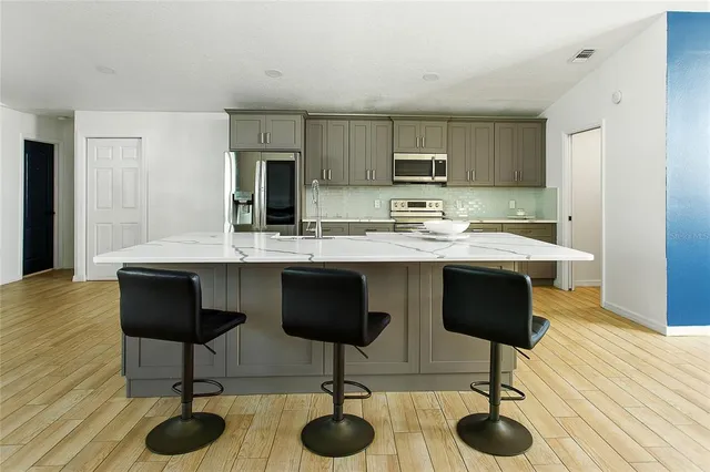 a kitchen with stainless steel appliances kitchen island granite countertop a table chairs sink and cabinets