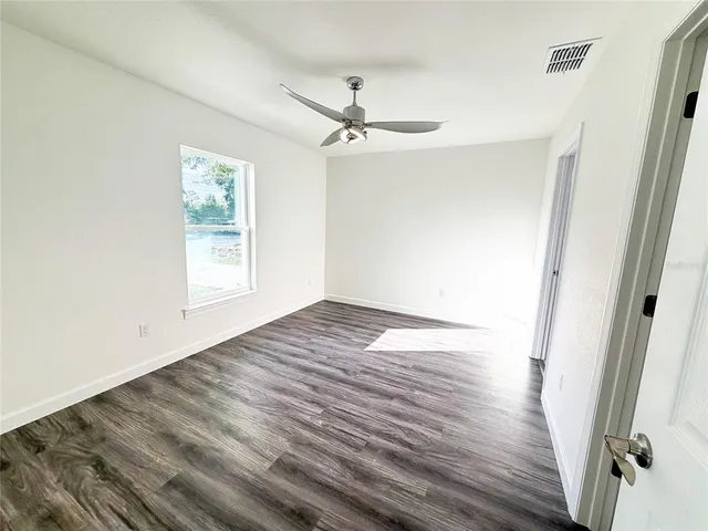 an empty room with wooden floor fan and windows