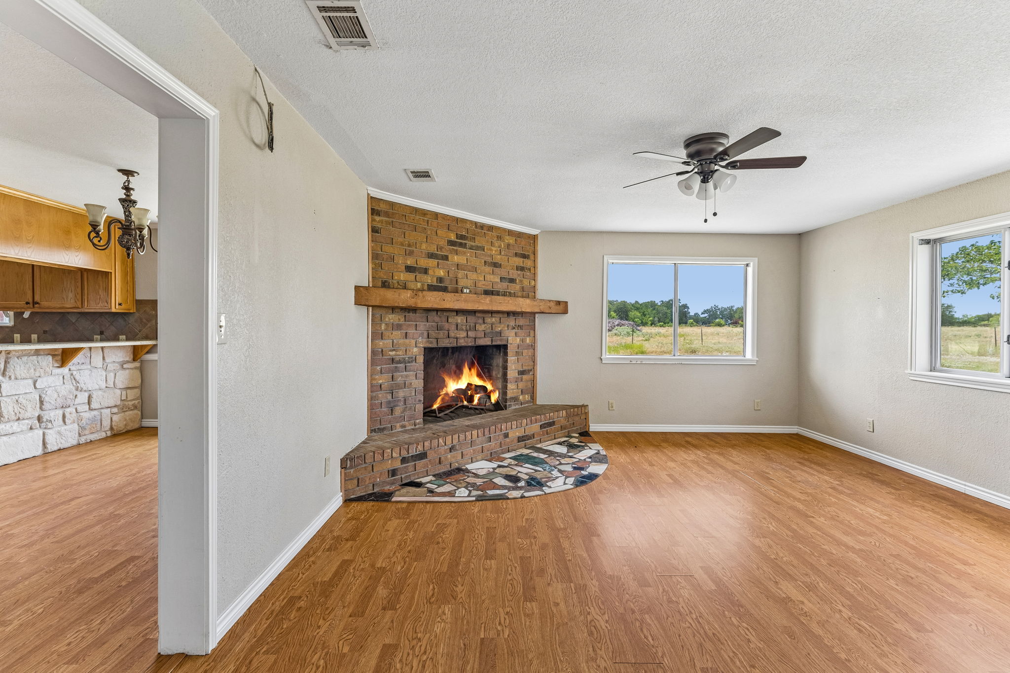 9765 A State Park Road Lockhart, TX 78644 - Photo 4 of 30 A corner brick fireplace with a rustic wood mantle anchors this inviting living space, offering warmth and a focal point.