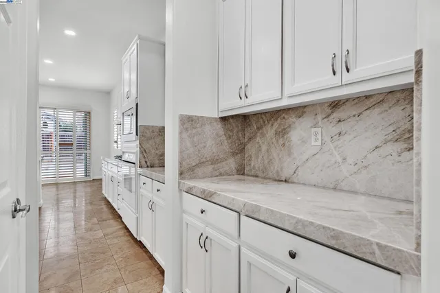 a large white kitchen with granite countertop a large counter top space appliances and cabinets