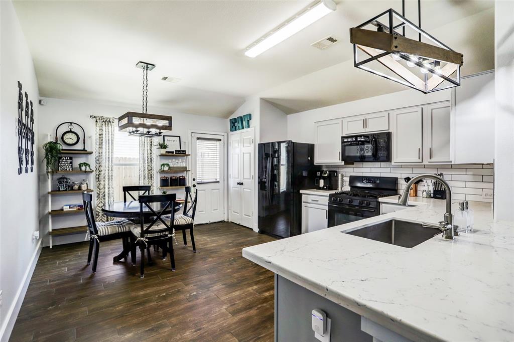 a kitchen with stainless steel appliances granite countertop a sink dishwasher a refrigerator a stove a dining table and chairs with wooden floor