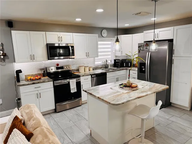 a kitchen with stainless steel appliances kitchen island granite countertop a sink a stove a refrigerator and island with wooden floor