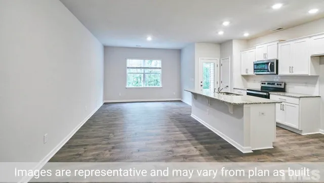a large white kitchen with kitchen island a sink wooden floor and black appliances