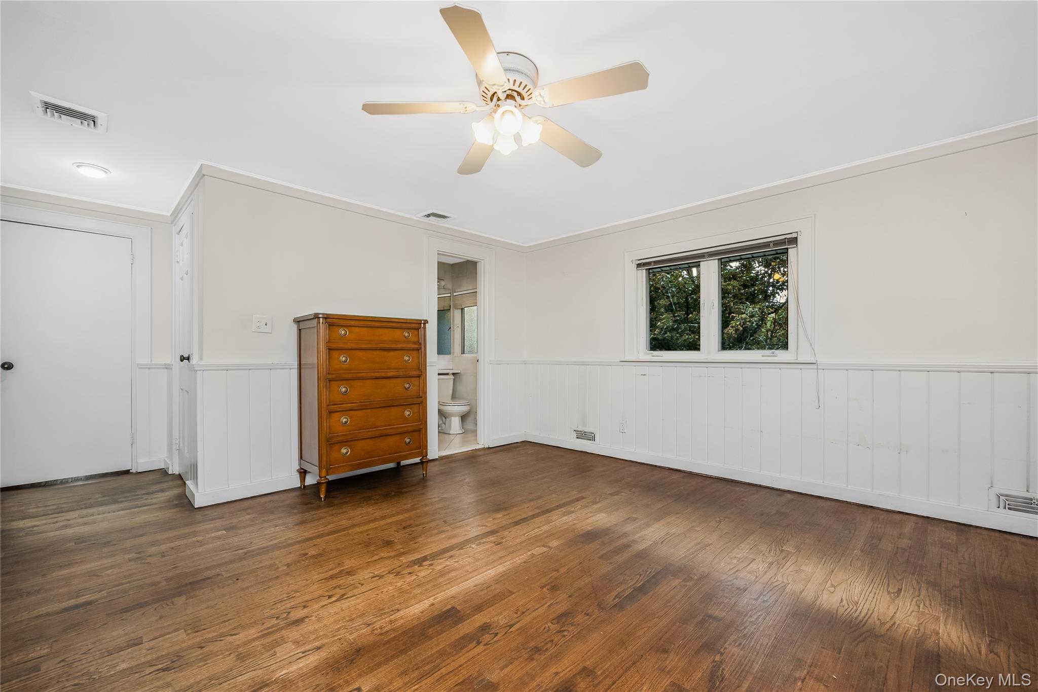 29 Randy Lane Plainview, NY 11803 - Photo 27 of 38 Wood-finish flooring, white paneled wainscoting, and a ceiling fan with integrated lighting and access to the primary bath
