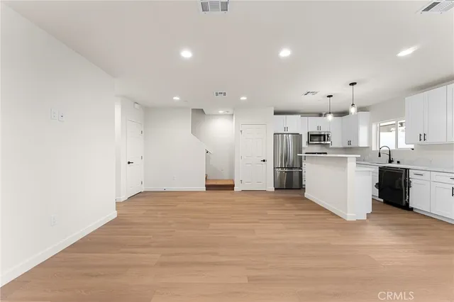 a view of a kitchen with kitchen island a sink wooden floor and stainless steel appliances