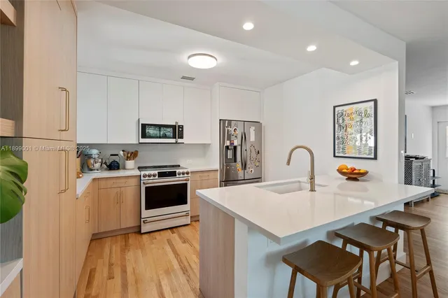 a kitchen with stainless steel appliances a stove a sink a microwave a refrigerator and white cabinets with wooden floor