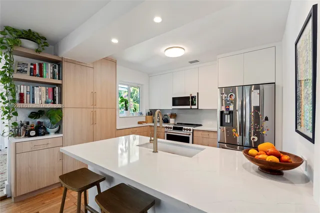 a kitchen with stainless steel appliances a stove a refrigerator a sink a dining table and chairs with wooden floor