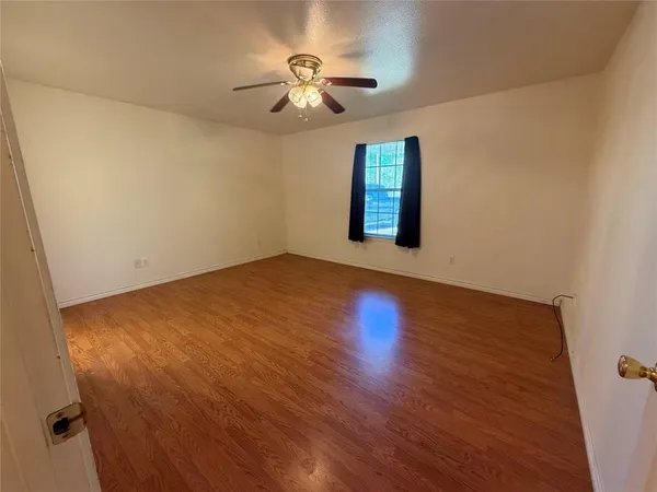 an empty room with wooden floor chandelier fan and windows