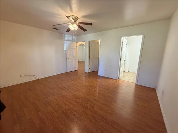 an empty room with wooden floor chandelier fan and windows