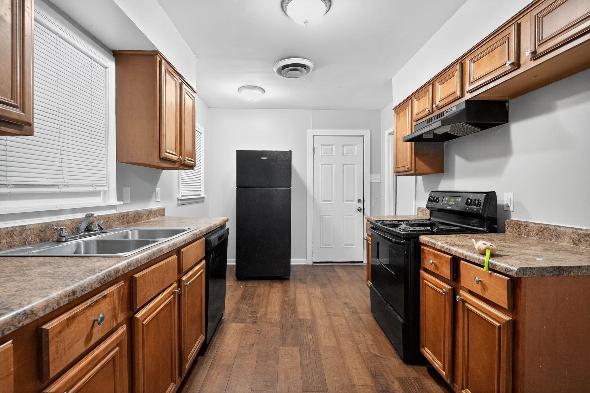 177 East Raines Road Memphis, TN 38109 - Photo 16 of 32 Kitchen featuring black appliances, dark wood-style floors, brown cabinets, under cabinet range hood, and dark countertops