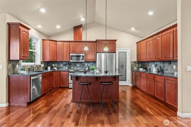 a kitchen with stainless steel appliances kitchen island granite countertop wooden floors wooden cabinets and sink