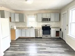 a kitchen with stainless steel appliances granite countertop a stove top oven a refrigerator and white cabinets with wooden floor