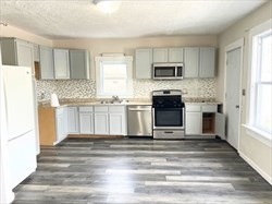 67-69 Loring Street Lowell, MA 01851 - Photo 3 of 16 a kitchen with stainless steel appliances granite countertop a stove top oven a refrigerator and white cabinets with wooden floor