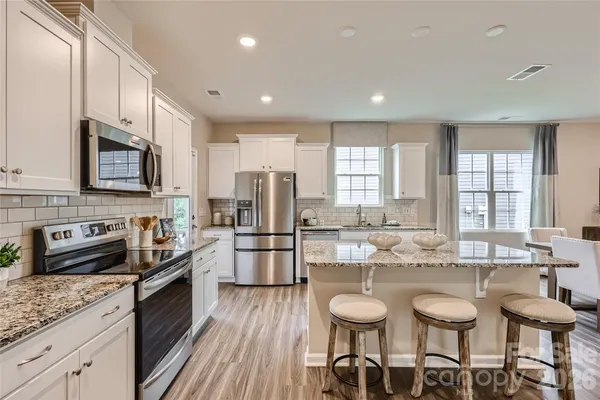 a kitchen with stainless steel appliances granite countertop a stove top oven a sink dishwasher a dining table and chairs with wooden floor