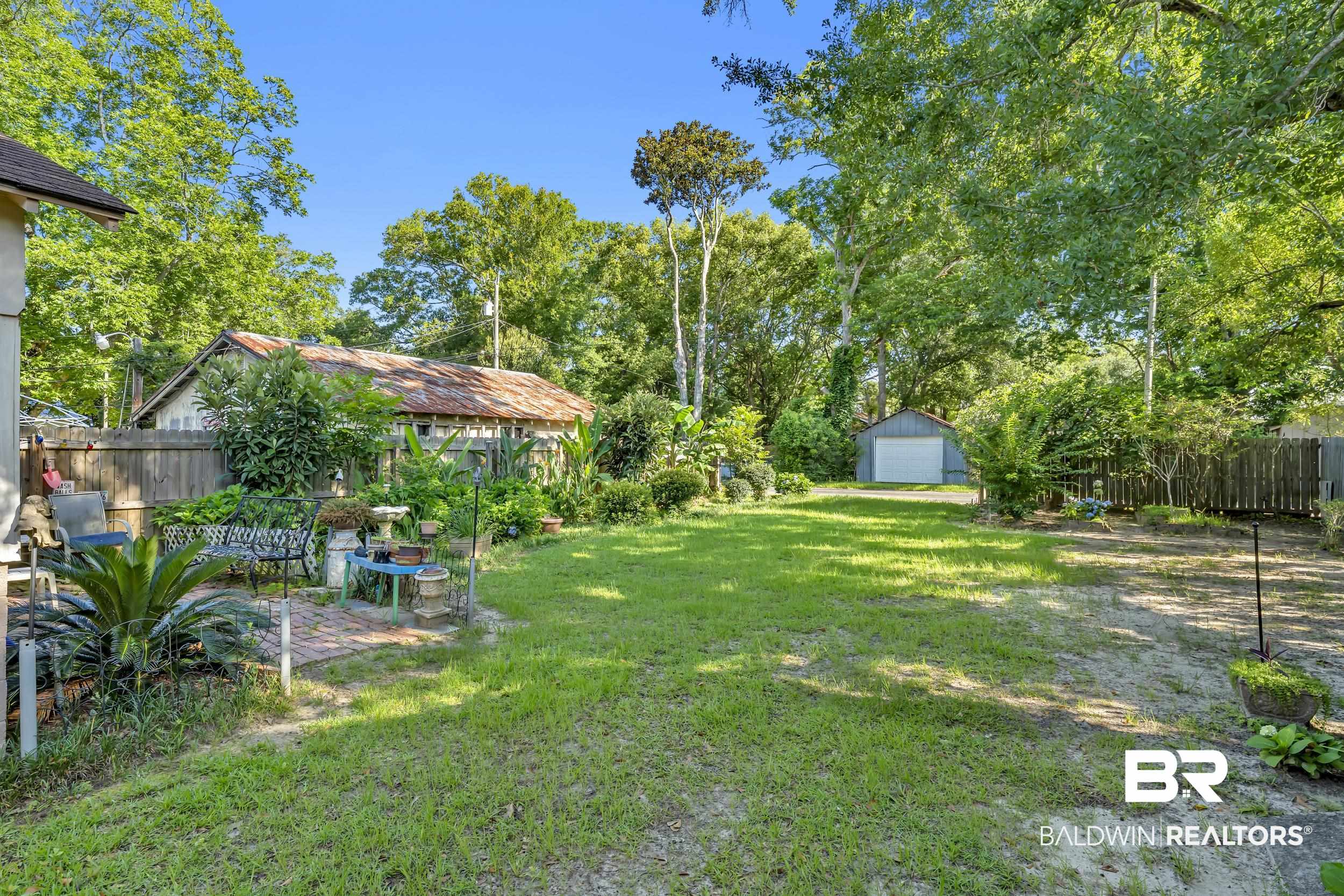 304 West Myrtle Avenue Foley, AL 36535 - Photo 26 of 29 Expansive backyard featuring a large grassy area, mature trees, a brick patio, and a detached shed with a roll-up door