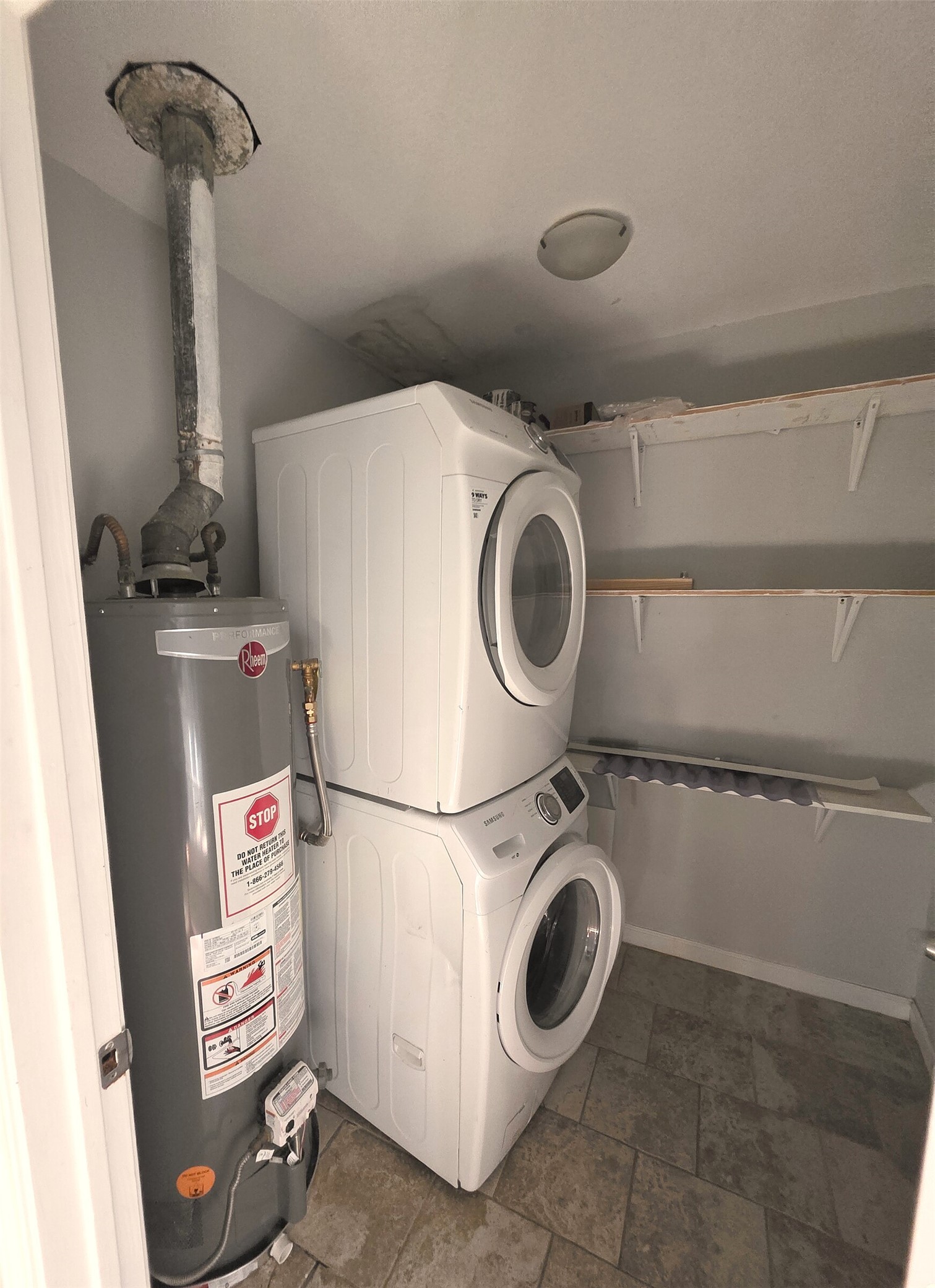 703 Castle Ridge Road, Unit B Austin, TX 78746 - Photo 17 of 18 A dedicated utility space includes stacked laundry appliances, open shelving, and tile flooring.