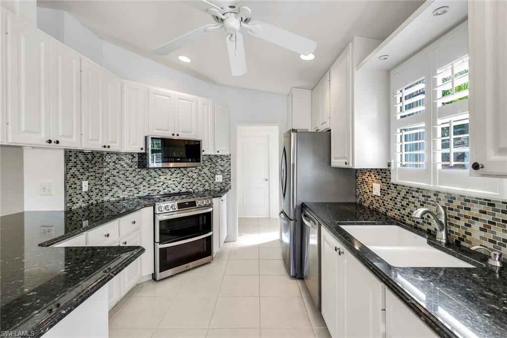 3025 Futuna Lane Naples, FL 34119 - Photo 16 of 46 Kitchen featuring dark stone countertops, white cabinets, stainless steel appliances, a ceiling fan, and light tile patterned floors